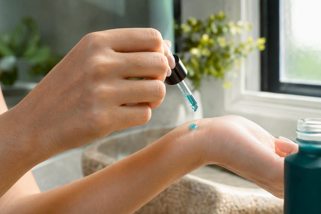 Hand dispensing blue peptide serum drop on skin