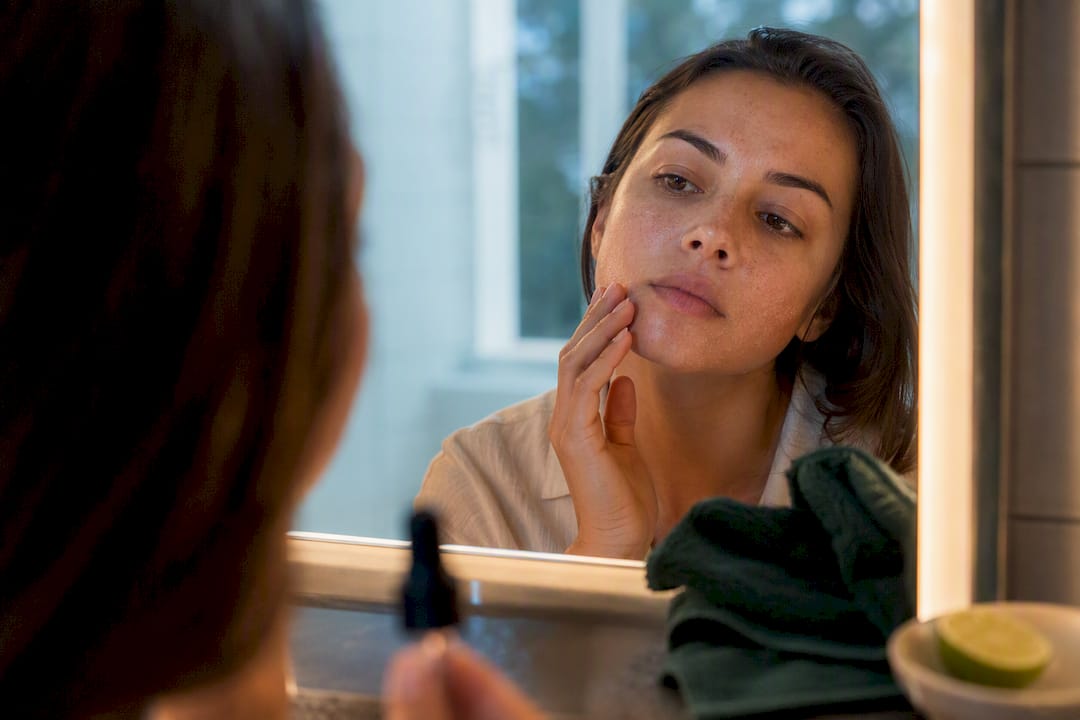 Person inspecting dry, flaky cheek in mirror